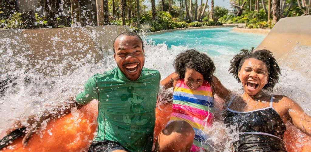 Family enjoying fun on a water slide with splashing water and smiling faces in a sunny outdoor pool setting